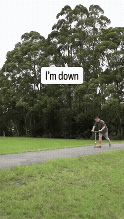 A Man Is Riding A Scooter Down A Path With Trees In The Background And A Sign That Says I 'M Down GIF