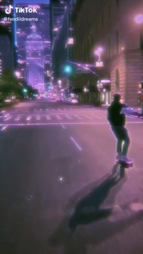 A Man Is Riding A Skateboard Down A Street At Night . GIF