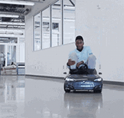A Man Is Riding A Small Blue Car In A Hallway . GIF