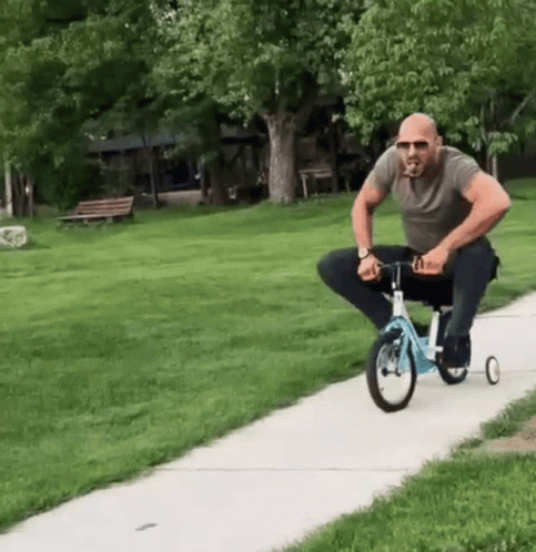 A Man Is Riding A Tricycle Down A Sidewalk GIF