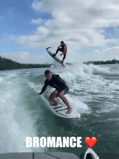A Man Is Riding A Wave On A Surfboard With The Word Bromance Written Below Him GIF