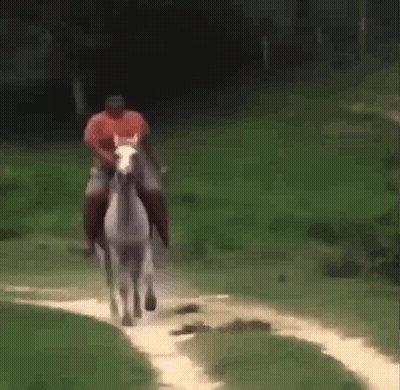 A Man Is Riding A White Horse On A Dirt Road . GIF