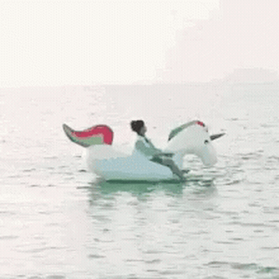 A Man Is Riding An Inflatable Unicorn In The Water . GIF