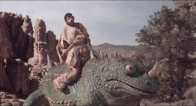 A Man Is Riding On The Back Of A Green Dinosaur With Horns GIF