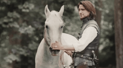 A Man Is Riding On The Back Of A White Horse In The Woods . GIF