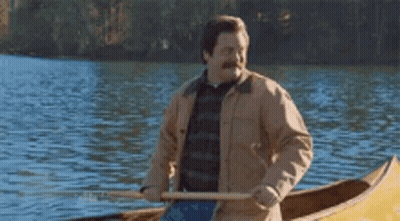A Man Is Rowing A Canoe On A Lake With A Paddle . GIF