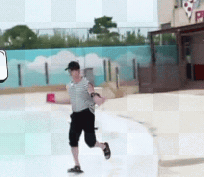 A Man Is Running Across A Swimming Pool While Holding A Red Cup . GIF
