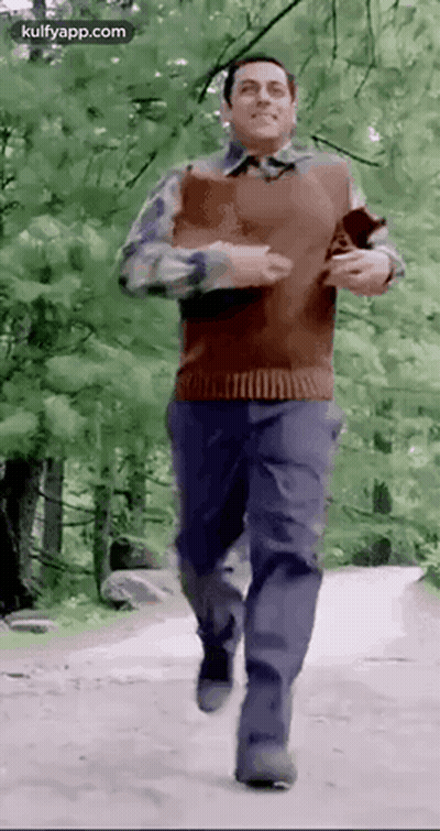 A Man Is Running Down A Dirt Road In The Woods . GIF