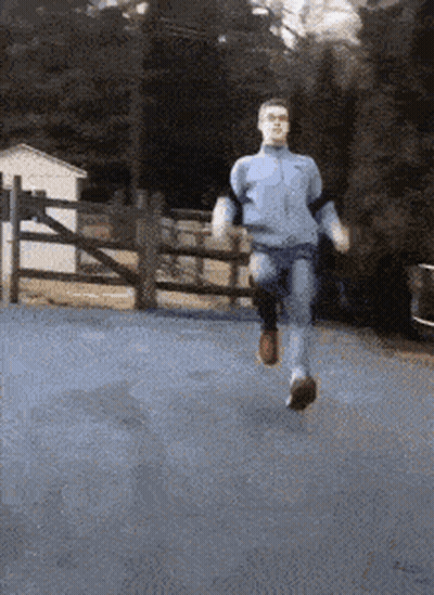 A Man Is Running Down A Road In Front Of A Fence GIF
