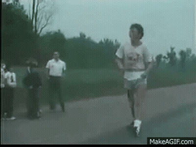 A Man Is Running Down A Road With A Group Of People Watching . GIF