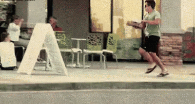 A Man Is Running Down A Sidewalk Holding A Box Of Pizza . GIF