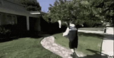 A Man Is Running Down A Sidewalk In A Yard . GIF