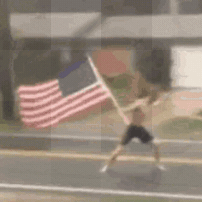 A Man Is Running Down A Street While Holding An American Flag . GIF