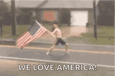 A Man Is Running Down A Street With An American Flag . GIF