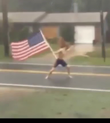 A Man Is Running Down The Street With An American Flag GIF