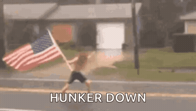 A Man Is Running Down The Street With An American Flag In His Hand . GIF