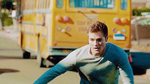 A Man Is Running In Front Of A Yellow School Bus . GIF