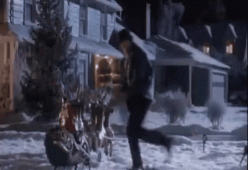 A Man Is Running In The Snow In Front Of A House With A Sleigh Full Of Reindeer . GIF
