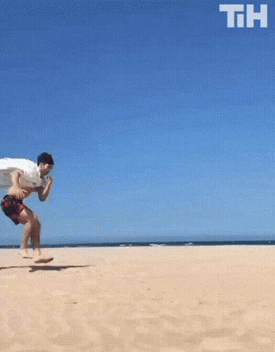 A Man Is Running On A Sandy Beach With The Letters Th Above Him GIF