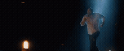 A Man Is Running Through A Dark Room With A Blue Light Coming From Behind Him . GIF