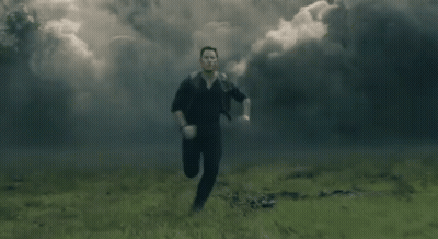 A Man Is Running Through A Field With Smoke Coming Out Of It . GIF