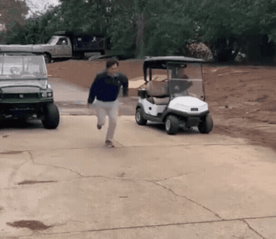 A Man Is Running Towards A Golf Cart That Is Parked In A Driveway GIF