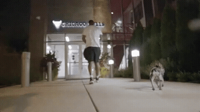 A Man Is Running With A Dog In Front Of A Building That Says Chicago On It GIF