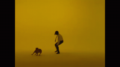 A Man Is Running With A Dog In Front Of A Yellow Wall GIF