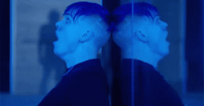 A Man Is Screaming In Front Of A Mirror And His Reflection Is Visible . GIF