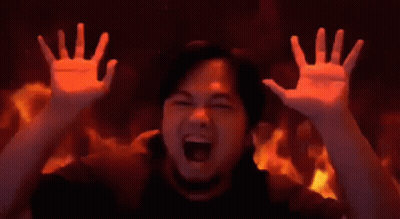 A Man Is Screaming In Front Of A Wall Of Fire . GIF