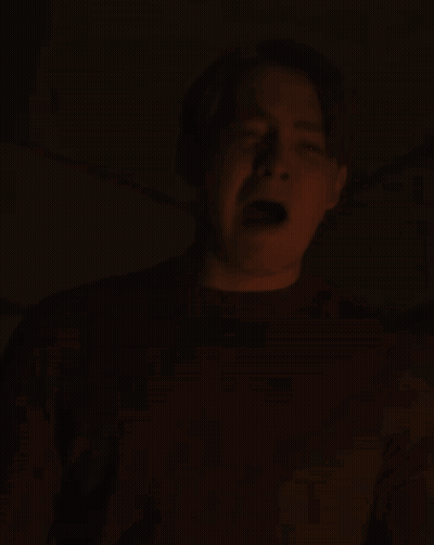 A Man Is Screaming In The Dark With His Mouth Open And His Tongue Sticking Out GIF