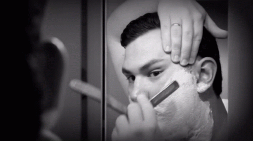 A Man Is Shaving His Face With A Razor In A Black And White Photo GIF