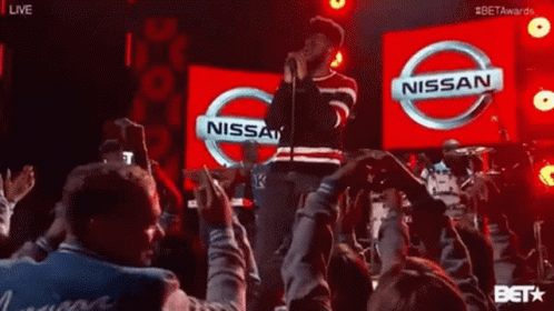 A Man Is Singing In Front Of A Nissan Sign GIF