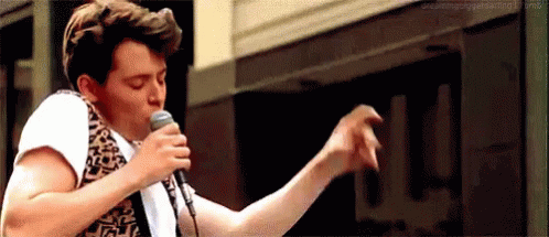 A Man Is Singing Into A Microphone And Dancing . GIF