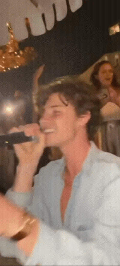 A Man Is Singing Into A Microphone At A Party In A Dark Room . GIF
