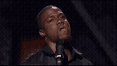 A Man Is Singing Into A Microphone In A Dark Room GIF