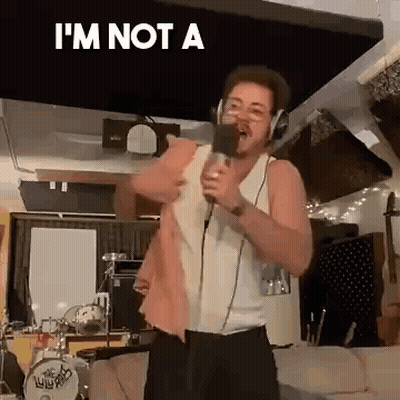 A Man Is Singing Into A Microphone In A Living Room While Wearing Headphones . GIF