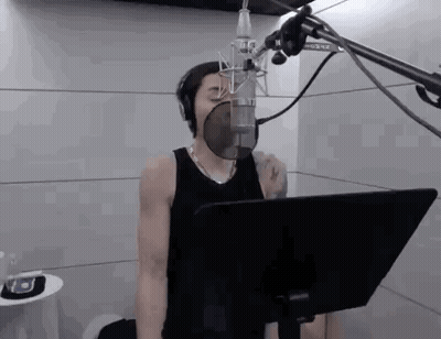 A Man Is Singing Into A Microphone In A Recording Studio While Wearing Headphones . GIF