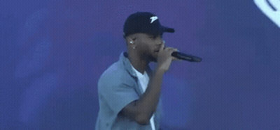 A Man Is Singing Into A Microphone In Front Of A Blue Background With A Heart . GIF