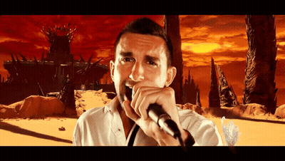 A Man Is Singing Into A Microphone In Front Of A Castle GIF