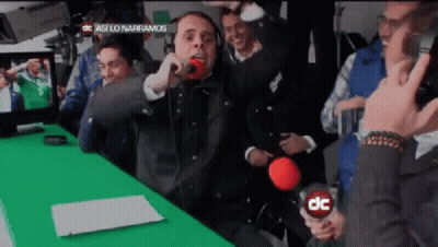 A Man Is Singing Into A Microphone In Front Of A Green Screen That Says Dc GIF