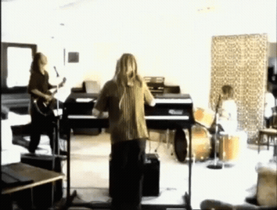 A Man Is Singing Into A Microphone In Front Of A Piano In A Room With Other People Playing Instruments . GIF