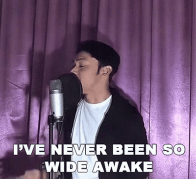 A Man Is Singing Into A Microphone In Front Of A Pink Curtain . GIF