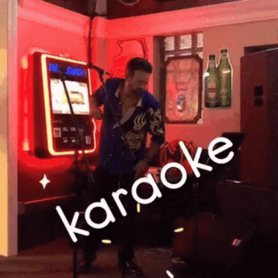 A Man Is Singing Into A Microphone In Front Of A Sign That Says " Karaoke " GIF