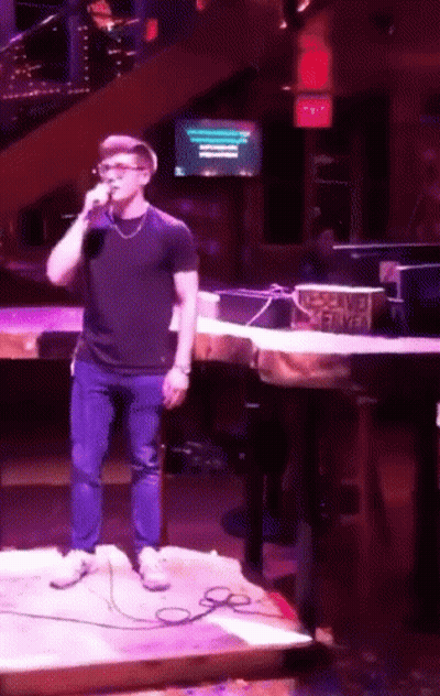 A Man Is Singing Into A Microphone In Front Of A Sign That Says No Smoking Served GIF