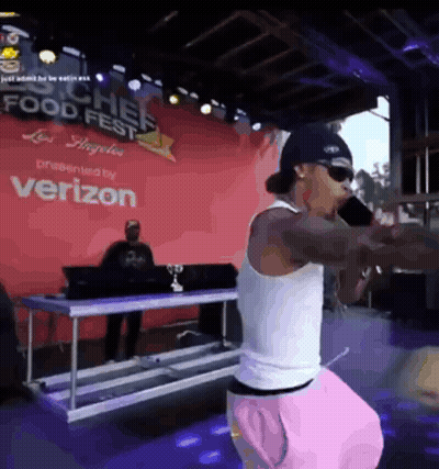 A Man Is Singing Into A Microphone In Front Of A Verizon Sign GIF