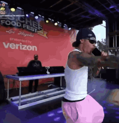A Man Is Singing Into A Microphone In Front Of A Verizon Sign GIF