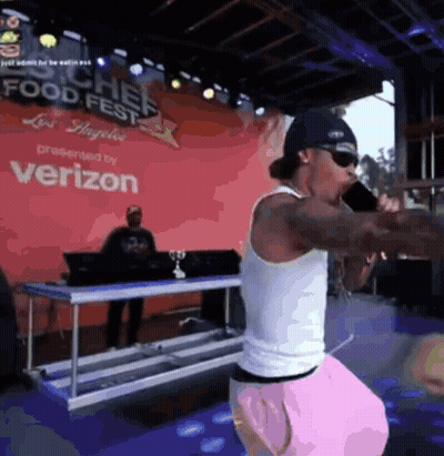 A Man Is Singing Into A Microphone In Front Of A Verizon Sign GIF