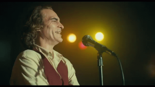 A Man Is Singing Into A Microphone In Front Of A Yellow Light . GIF