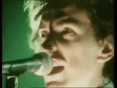 A Man Is Singing Into A Microphone On A Green Background . GIF